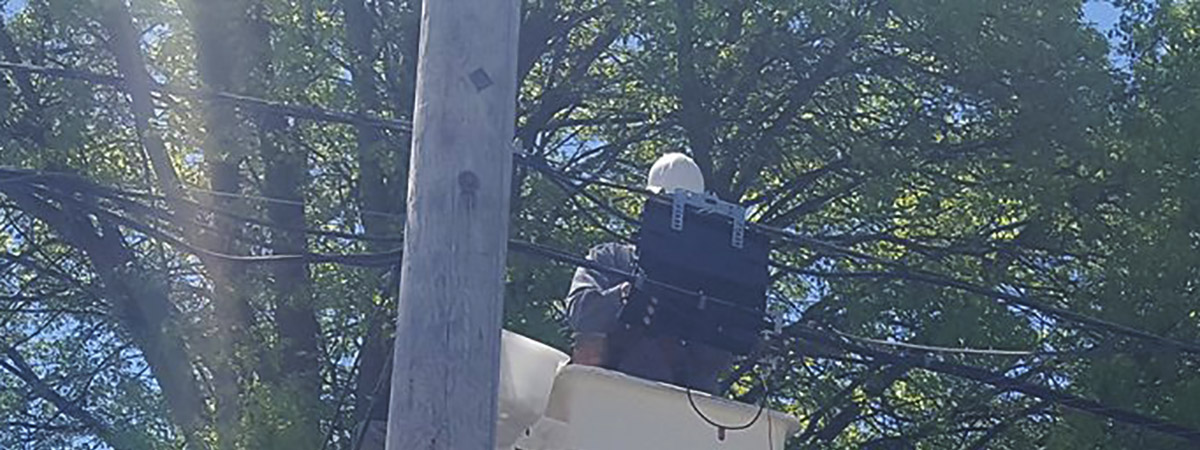 service technician in bucket working on lines at top of pole along street